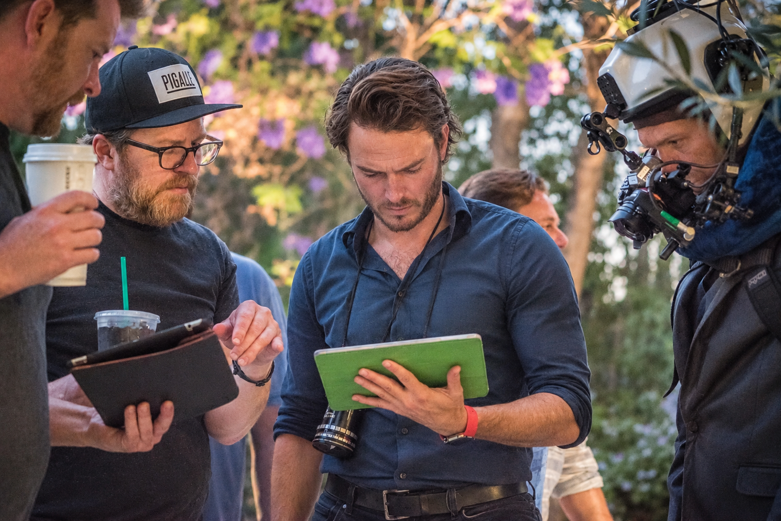 Pierre reviewing a tablet with the film crew beneath purple blossoms